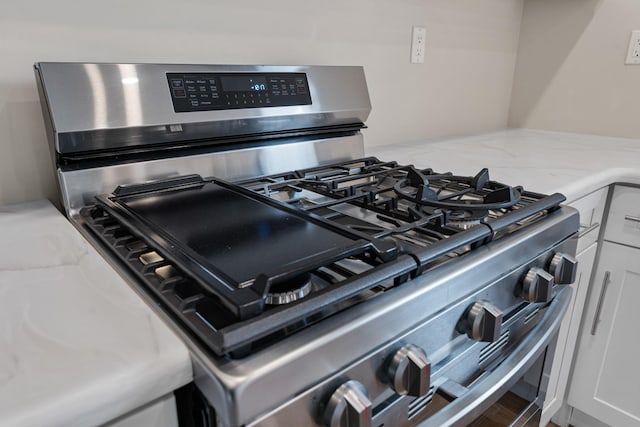 details featuring white cabinets, stainless steel gas stove, and light stone countertops