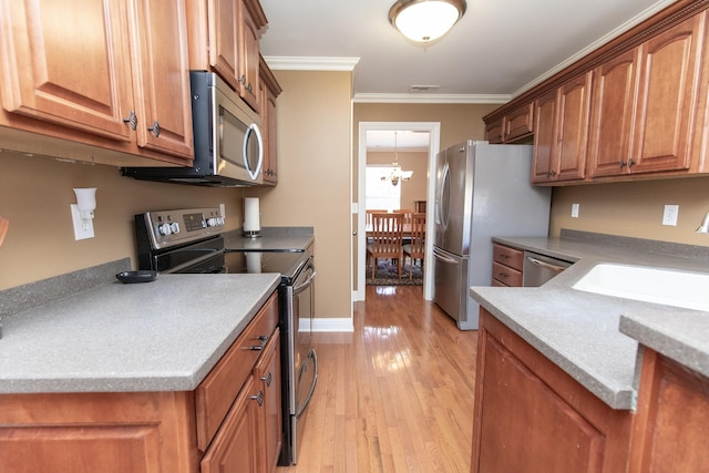 kitchen featuring sink, light hardwood / wood-style flooring, a notable chandelier, appliances with stainless steel finishes, and ornamental molding