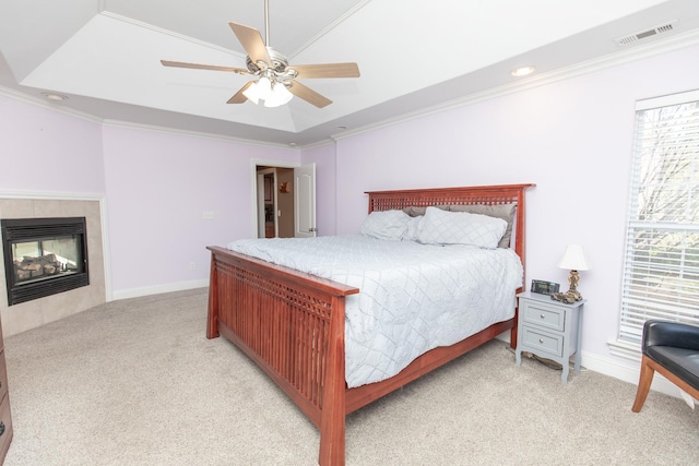 carpeted bedroom featuring ceiling fan, ornamental molding, a tile fireplace, and a tray ceiling