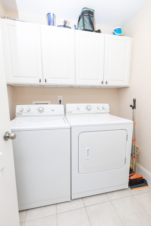 clothes washing area featuring washing machine and dryer, light tile patterned floors, and cabinets