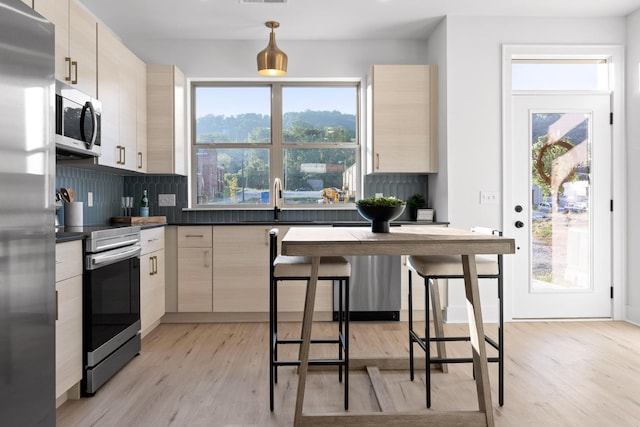 kitchen with tasteful backsplash, plenty of natural light, dark countertops, stainless steel appliances, and light wood-style floors