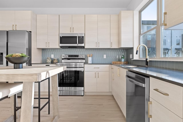 kitchen with appliances with stainless steel finishes, light wood-type flooring, a sink, and tasteful backsplash