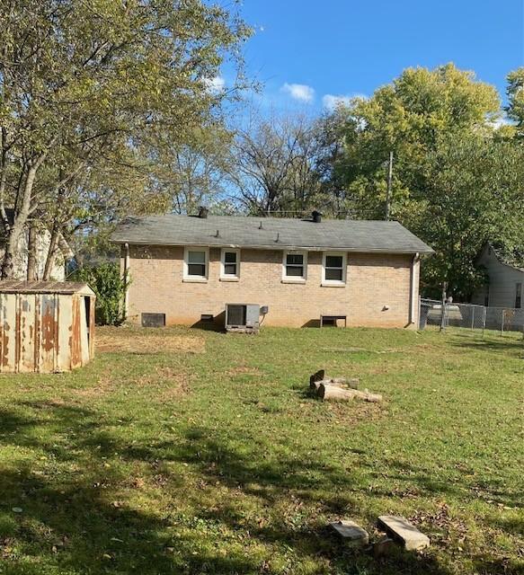 back of property featuring a yard, cooling unit, and a storage shed