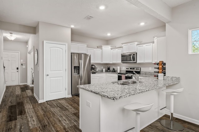 kitchen featuring white cabinetry, stainless steel appliances, light stone counters, a breakfast bar, and sink