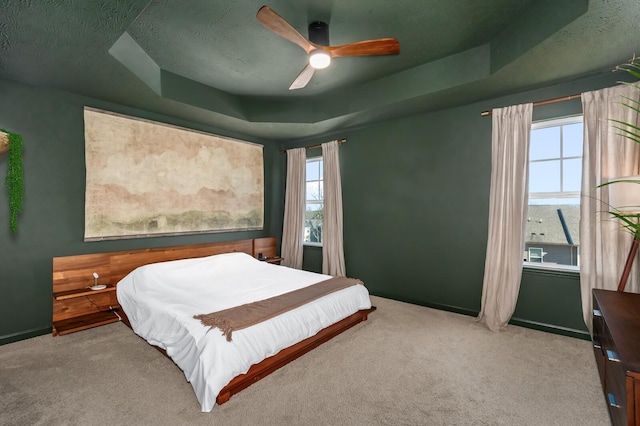 carpeted bedroom with ceiling fan, a tray ceiling, and a textured ceiling