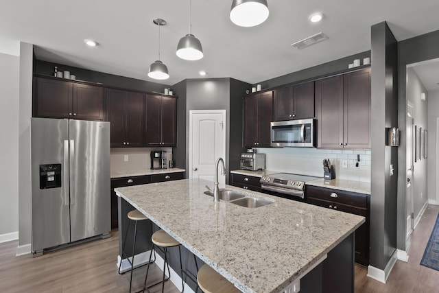 kitchen with sink, hanging light fixtures, stainless steel appliances, a center island with sink, and dark brown cabinets