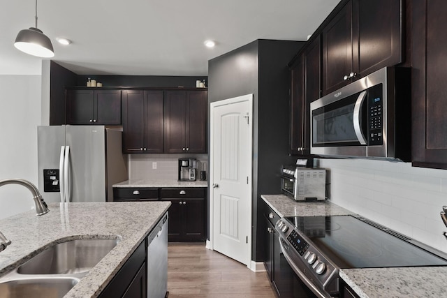 kitchen with light stone countertops, sink, backsplash, pendant lighting, and appliances with stainless steel finishes