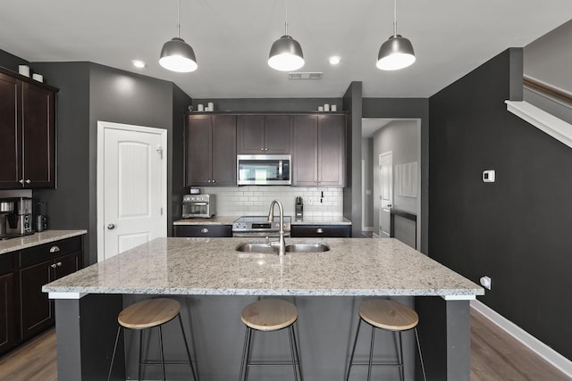 kitchen featuring tasteful backsplash, a center island with sink, decorative light fixtures, and appliances with stainless steel finishes