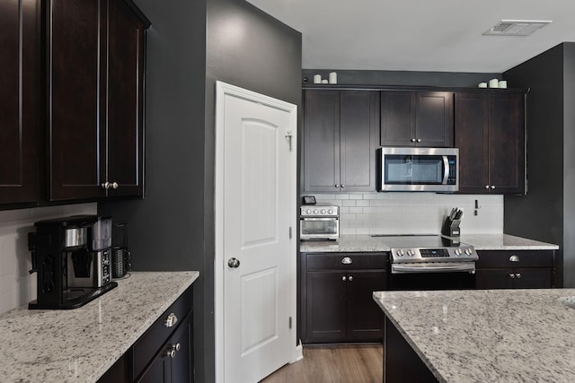 kitchen with backsplash, light hardwood / wood-style flooring, light stone countertops, appliances with stainless steel finishes, and dark brown cabinets