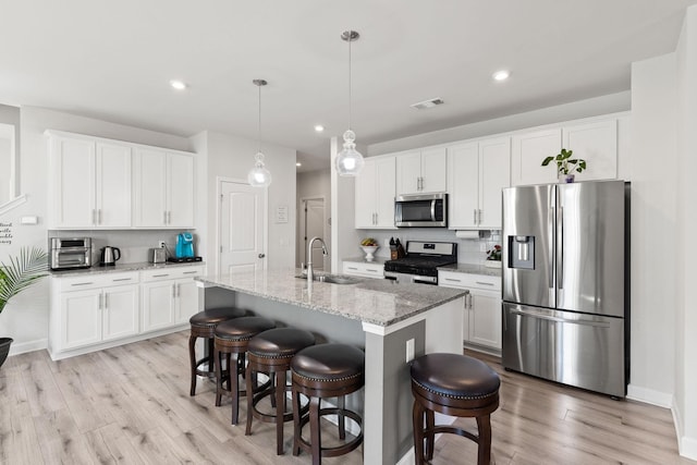 kitchen with stainless steel appliances, light stone counters, pendant lighting, a kitchen island with sink, and white cabinets