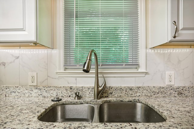 room details with white cabinetry, light stone counters, tasteful backsplash, and sink