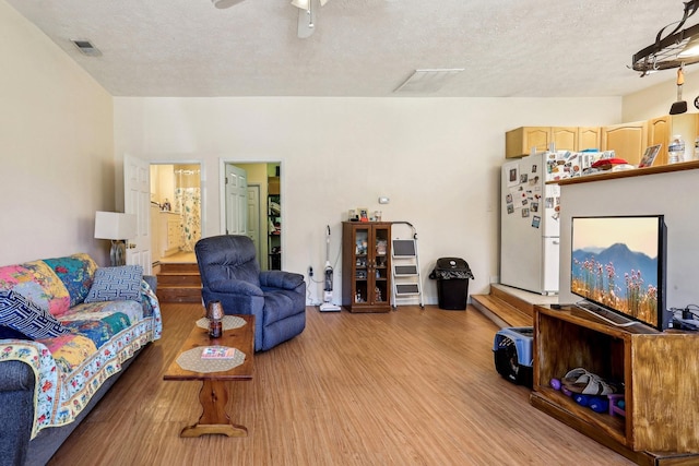 living room featuring light wood-type flooring, a textured ceiling, and ceiling fan