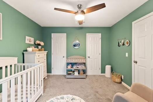 bedroom with ceiling fan, light colored carpet, and a crib