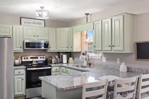 kitchen featuring kitchen peninsula, appliances with stainless steel finishes, a kitchen breakfast bar, light stone counters, and sink