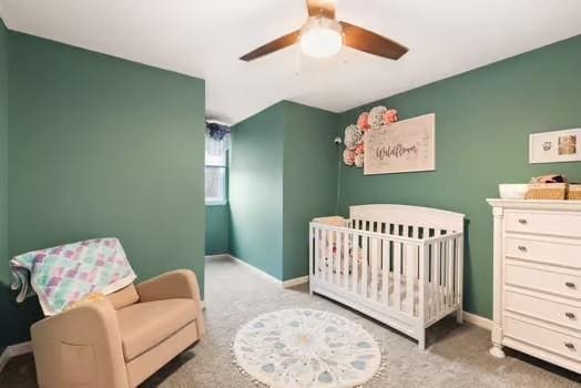 carpeted bedroom featuring ceiling fan and a crib