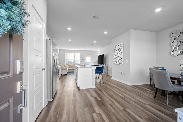 kitchen featuring hardwood / wood-style floors, a center island with sink, stainless steel fridge, a kitchen bar, and white cabinetry