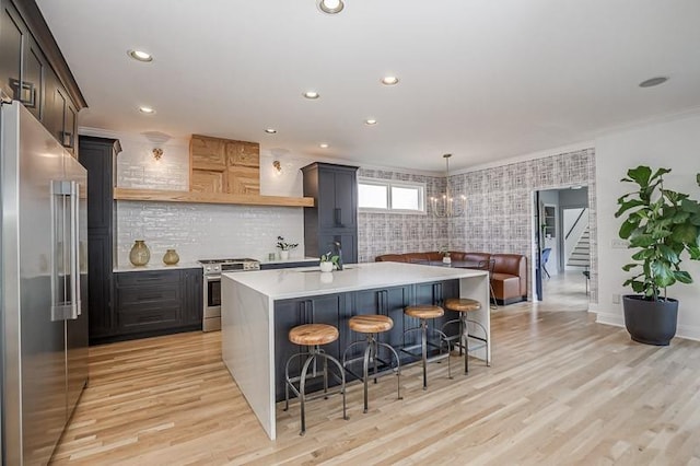 kitchen featuring crown molding, light hardwood / wood-style flooring, appliances with stainless steel finishes, dark brown cabinets, and a kitchen bar