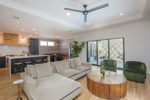 living room featuring a raised ceiling, light hardwood / wood-style flooring, ceiling fan, and crown molding