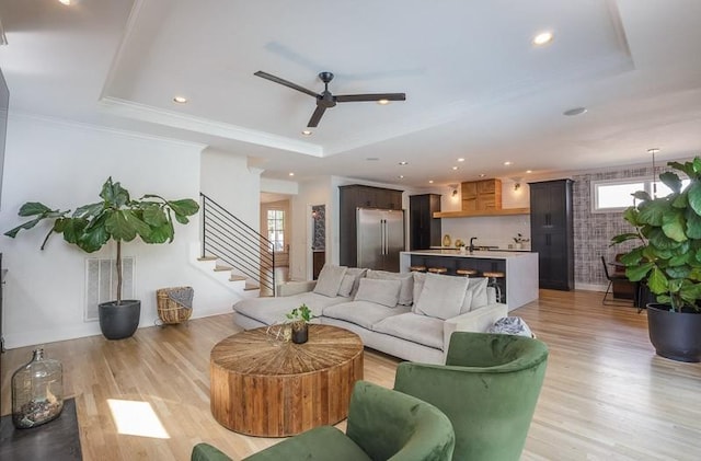 living room with light hardwood / wood-style floors, a raised ceiling, ceiling fan, and crown molding