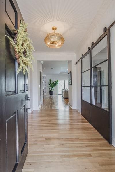 hall with a barn door, crown molding, and light hardwood / wood-style flooring