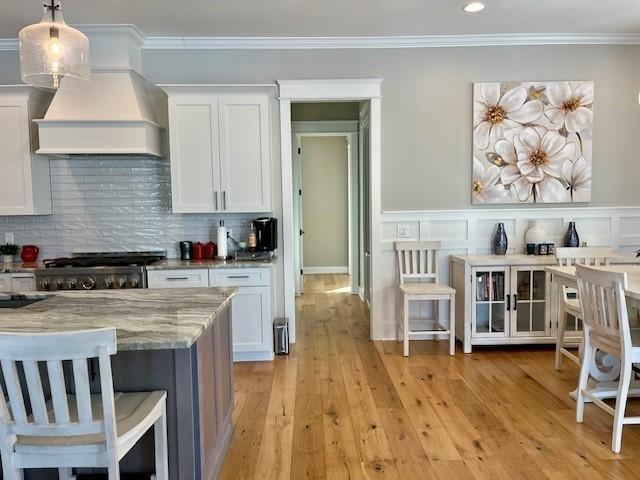 kitchen with light stone counters, light hardwood / wood-style floors, decorative light fixtures, white cabinets, and custom range hood