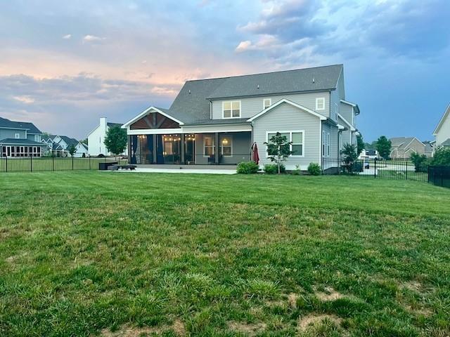 back house at dusk with a lawn and a sunroom