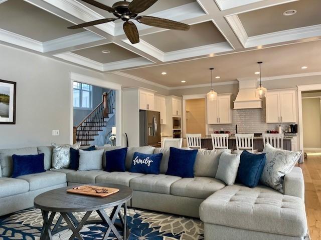 living room featuring ceiling fan, coffered ceiling, beamed ceiling, crown molding, and light hardwood / wood-style floors