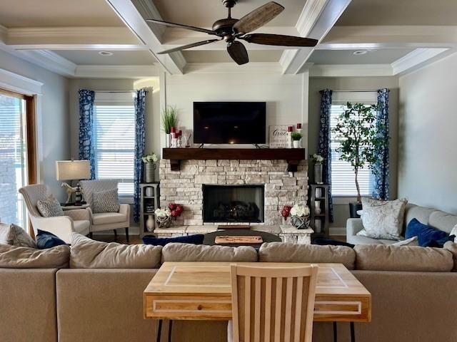 living room with coffered ceiling, ceiling fan, ornamental molding, a fireplace, and beam ceiling