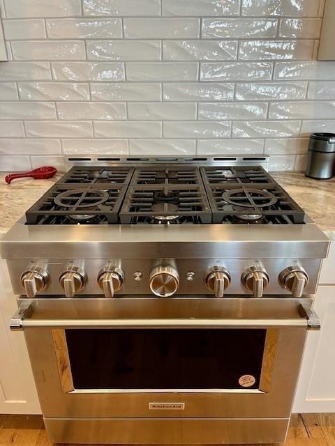 interior details featuring backsplash, white cabinetry, high end stainless steel range, and light stone counters