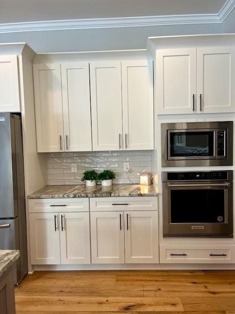 kitchen featuring light stone countertops, white cabinetry, backsplash, and appliances with stainless steel finishes