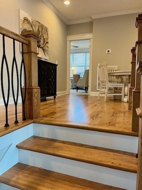 stairway with wood-type flooring, ornamental molding, and a fireplace