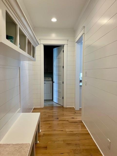 hall featuring wood-type flooring, washer / clothes dryer, ornamental molding, and wood walls