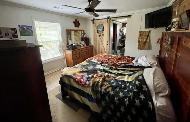 bedroom featuring a barn door, ceiling fan, crown molding, and light hardwood / wood-style floors