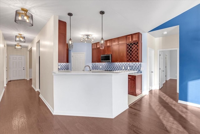 kitchen with kitchen peninsula, tasteful backsplash, sink, hardwood / wood-style floors, and hanging light fixtures