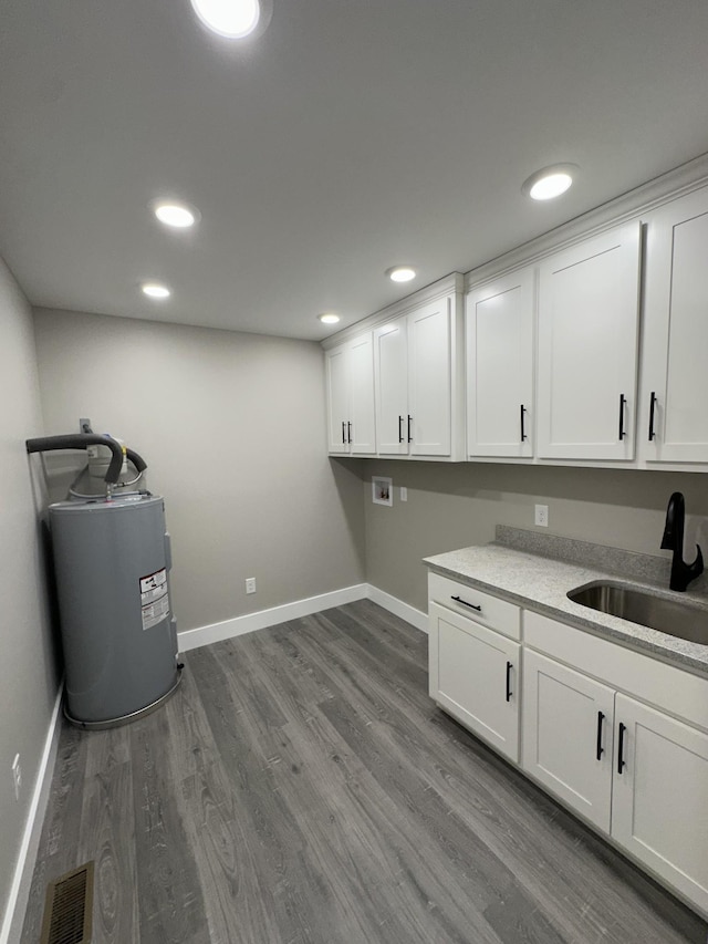 laundry area with cabinets, hookup for a washing machine, water heater, sink, and wood-type flooring