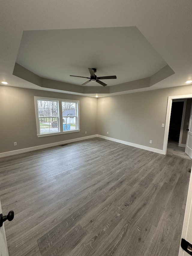 unfurnished room featuring a raised ceiling, ceiling fan, and dark wood-type flooring