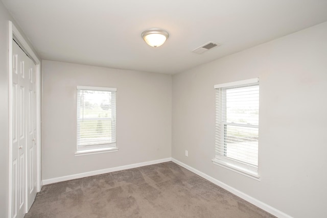 unfurnished bedroom featuring light carpet, a closet, and multiple windows