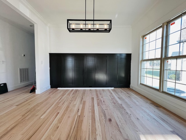 unfurnished dining area with light hardwood / wood-style floors, an inviting chandelier, a wealth of natural light, and ornamental molding