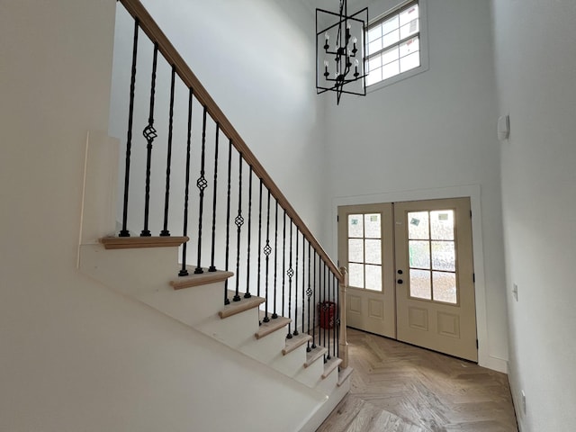 foyer featuring light parquet floors, french doors, a towering ceiling, and a chandelier