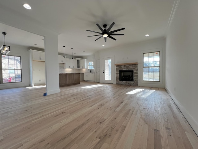 unfurnished living room with a stone fireplace, ceiling fan, ornamental molding, and light wood-type flooring