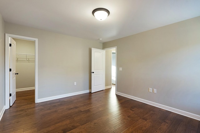 unfurnished bedroom featuring a walk in closet, dark wood-type flooring, and a closet