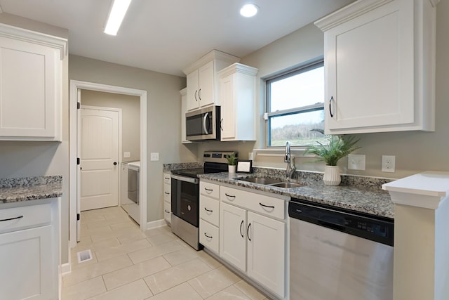 kitchen with appliances with stainless steel finishes, sink, light tile patterned floors, white cabinets, and washer / dryer