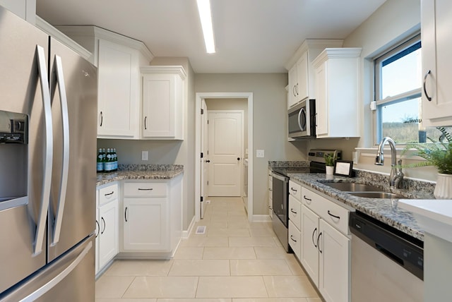 kitchen with sink, light stone countertops, light tile patterned floors, appliances with stainless steel finishes, and white cabinetry