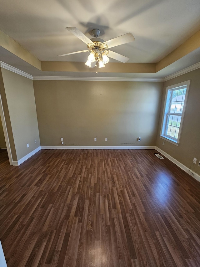 empty room with ceiling fan, a raised ceiling, ornamental molding, and dark wood-type flooring