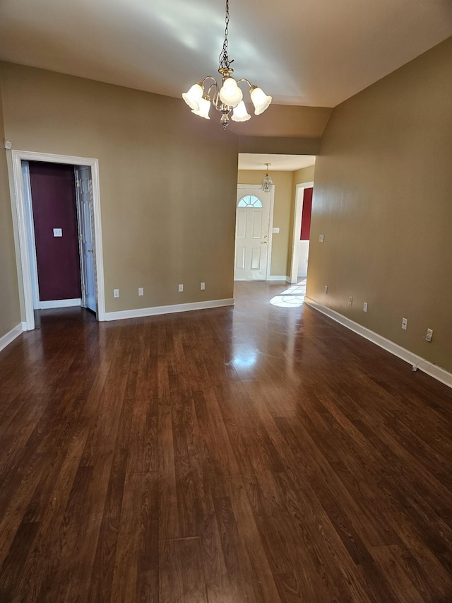 spare room featuring dark wood-type flooring and a chandelier