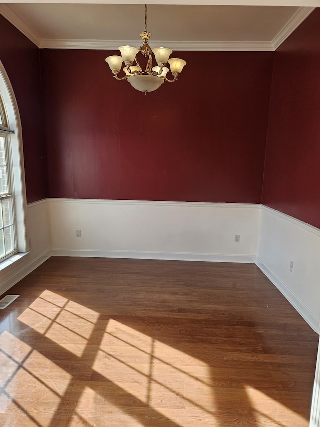 empty room with crown molding, hardwood / wood-style floors, and an inviting chandelier