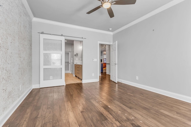 unfurnished bedroom featuring a barn door, ceiling fan, crown molding, and ensuite bathroom