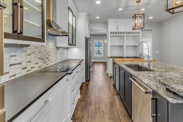 kitchen featuring appliances with stainless steel finishes, sink, wall chimney range hood, decorative light fixtures, and white cabinets