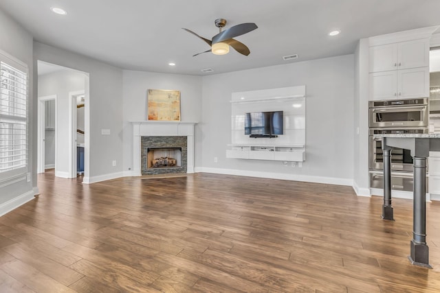 unfurnished living room with hardwood / wood-style floors, ceiling fan, and a stone fireplace