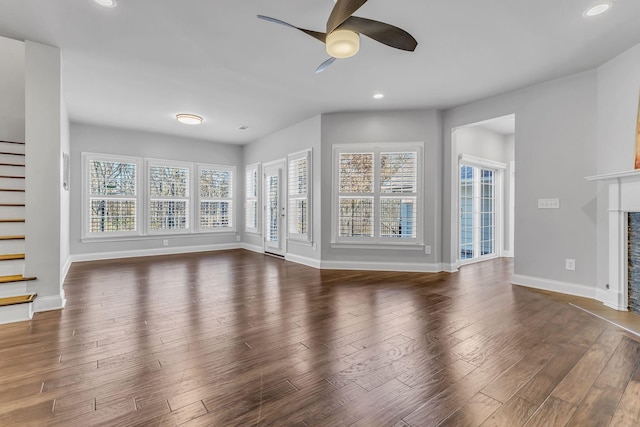 unfurnished living room featuring a stone fireplace, ceiling fan, and dark wood-type flooring